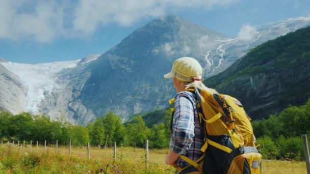 Μια δραστήρια γυναίκα με σακίδιο περπατάει μέσα από μια γραφική περιοχή στα βουνά προς τον παγετώνα. Φύση της Νορβηγίας — Αρχείο Βίντεο