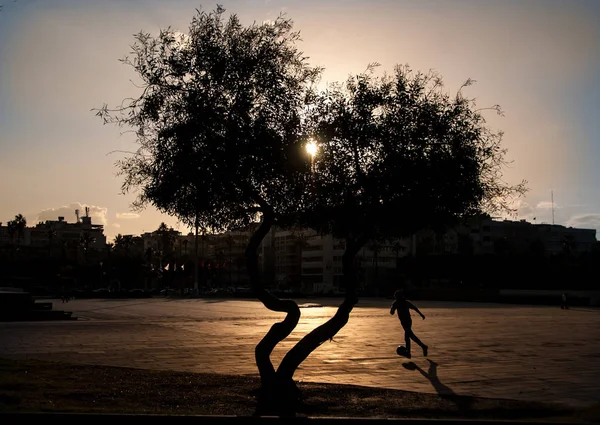 Αγόρι παίζει ποδόσφαιρο στο ηλιοβασίλεμα από την ημέρα — Φωτογραφία Αρχείου
