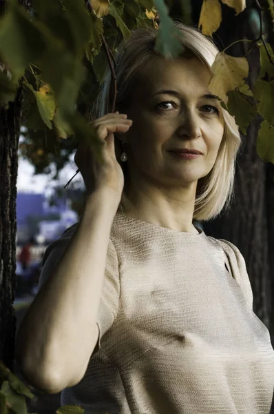 Блондинка середнього віку в літньому парку на заході сонця на фоні дерева і зеленого листя — стокове фото