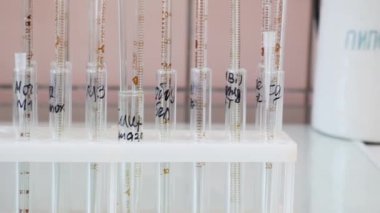 Cam test tüplerine elle yazılmış yazılar. Tribündeki test tüpleri eşit hizada duruyor. Kamera sağdan sola doğru sorunsuzca hareket eder. Yakın plan. Parlak beyaz ışık.