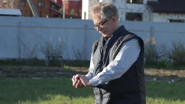 Ein älterer Mann mit Brille zerquetscht die Erde in seinen Händen. — Stockvideo