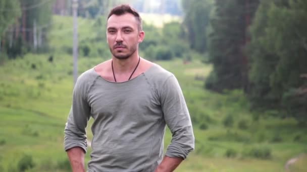 Un jeune homme se tient dans le fond d'une forêt verte et regarde . — Video