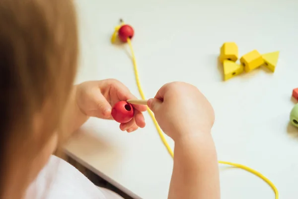 Çocuk ipin ucuna boncuk takıyor. Boncuk dizme aktivitesi. Güzel motor beceri geliştirme. Erken eğitim, Montessori Metodu. Bilişsel beceriler, çocuk gelişimi. Bebeğin ellerini kapayın. Bağlama, iplik etkinlikleri.  