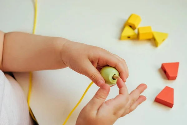 Çocuk ipin ucuna boncuk takıyor. Boncuk dizme aktivitesi. Güzel motor beceri geliştirme. Erken eğitim, Montessori Metodu. Bilişsel beceriler, çocuk gelişimi. Bebeğin ellerini kapayın. Bağlama, iplik etkinlikleri. 