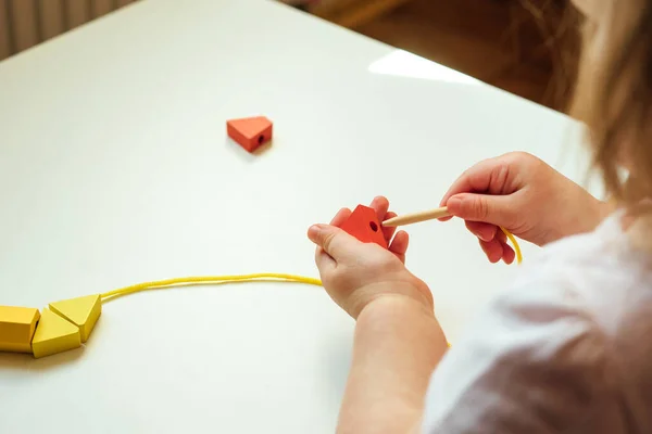 Child putting beads on a string. Bead stringing activity. Fine motor skills development. Early education, Montessori Method. Cognitive skills, children development. Close up of baby's hands. Lacing, threading activities.