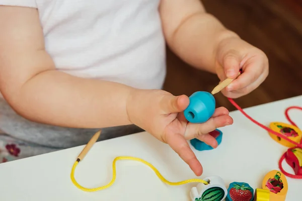 Çocuk ipin ucuna boncuk takıyor. Boncuk dizme aktivitesi. Güzel motor beceri geliştirme. Erken eğitim, Montessori Metodu. Bilişsel beceriler, çocuk gelişimi. Bebeğin ellerini kapayın. Bağlama, iplik etkinlikleri. 