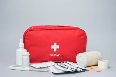 Medical first aid kit with medicine and pills. Isolated on gray background. Red bag with medical equipment and medications for emergency. clipart