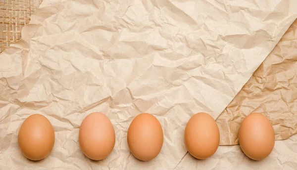 Fresh brown hen\'s eggs on wrinkled craft paper. Eco-friendly egg production. Bakery ingredients. Organic chicken eggs - fresh from producer. Trend of minimalism, top view. Free space for text.