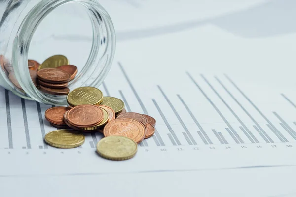 İçinde para olan cam kavanoz, grafikler üzerine kumbaradan dökülen paralar. Az para ya da az maaş. Tasarruf, kriz, iflas kavramı.