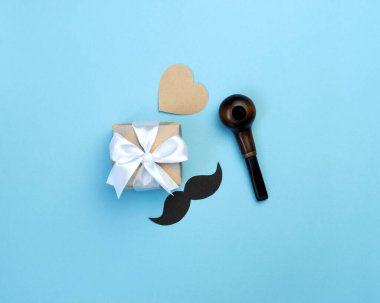 Babalar Günü kompozisyonun kutlu olsun. Hediye kutusu, siyah bıyık, mavi arka planda boru ve kalp. Babam için tebrik kartı. Üst görünüm düzlüğü.