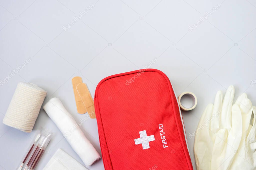 First aid kit red bag with medical equipment and medications for trauma and injuries treatment. Top view flat lay on gray background. Copy space.