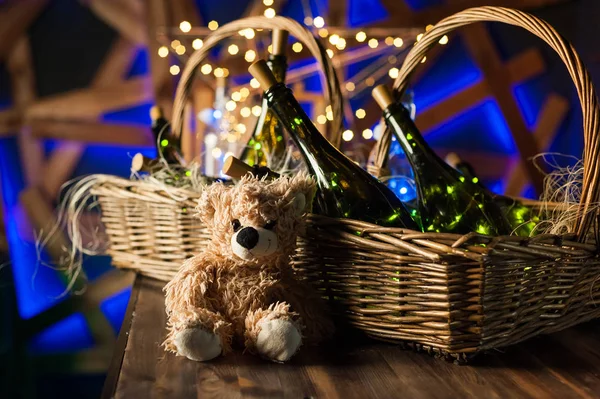 Teddy bear, champagne bottle with Christmas basket, gold garland — Stock Photo, Image