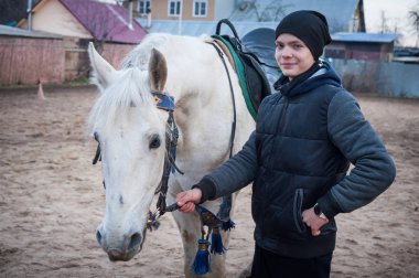 Yarış pistinde beyaz bir atla yürüyen bir genç.