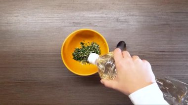 Kadın eli, otlarla sarımsağı bir kasede karıştırır. Yukarıdan görünüşü