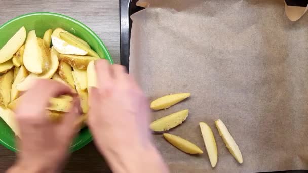 En man lägger rå potatis på en bakplåt. Smaksatt med salt, vitlök och peppar. Utsikten uppifrån. — Stockvideo