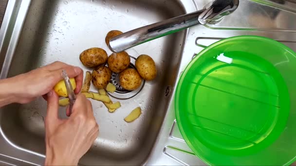 Καθαρισμός πατάτας με τα χέρια στον νεροχύτη της κουζίνας — Αρχείο Βίντεο