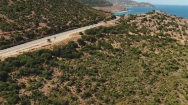 Denize yakın bir yolda kırmızı bir araba sürüşünün üst hava görüntüsü. Plajda ve sahil şeridindeki araçların insansız hava aracı görüntüleri..