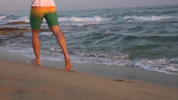 Un hombre corre en zapatillas en una playa de arena junto al mar. Moción lenta , — Vídeos de Stock