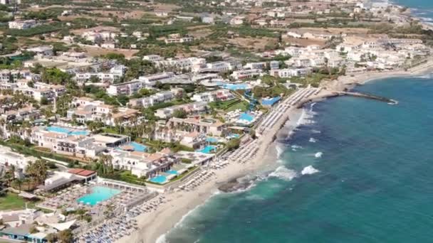 Drone aéreo de la costa de Anissaras cerca de Hersonissos en la isla histórica famosa de Creta Grecia con las playas de las piscinas del hotel y las olas mediterráneas del mar — Vídeos de Stock