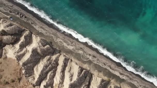 Odgórny widok z lotu ptaka turkusowe fale niebieskiego oceanu łamanie na brzegu dziewiczej tropikalnej plaży piasku Santorini — Wideo stockowe