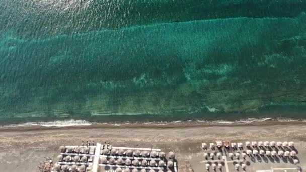Пляж с зонтиками и лежаками на берегу бирюзового моря, Греция Санторини — стоковое видео