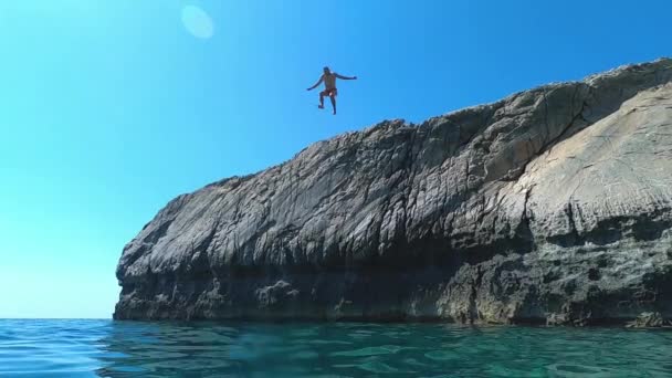 O homem salta de um penhasco para o mar em câmara lenta. Divertindo-se no verão no oceano Índico cristalino — Vídeo de Stock