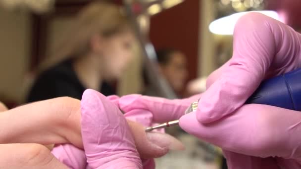 Close-up shot of hardware manicure in a beauty salon. Manicurist is applying electric nail file drill for trim cuticles on female fingers — Stock Video