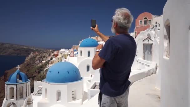 Hombre maduro de mediana edad feliz tomando fotos usando el teléfono inteligente en el café en Santorini — Vídeos de Stock