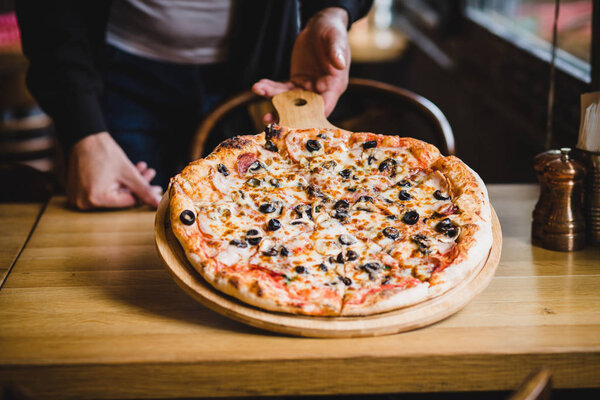 Pizza in the hands of the chef. Close-up on a dark background. Healthy fresh food. Italian Cuisine.