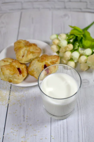 a glass of milk, cakes on a white plate and flowers on a wooden table