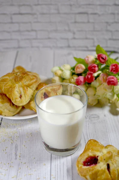a glass of milk, cakes on a white plate and flowers on a wooden table