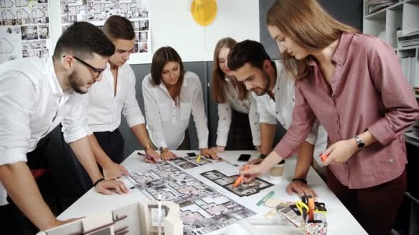 Four architects standing and planning around a table while looking down at blueprint 20s 4k. — Αρχείο Βίντεο