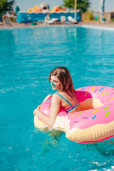 Giovane ragazza in spruzzato ciambella galleggiante a piscina — Foto Stock