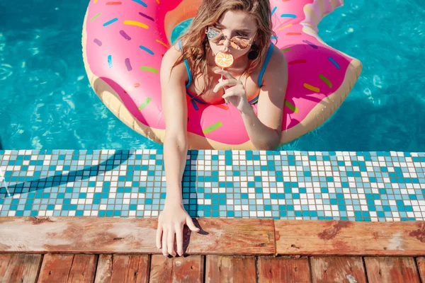 Jong meisje in bestrooid donut float bij zwembad — Stockfoto