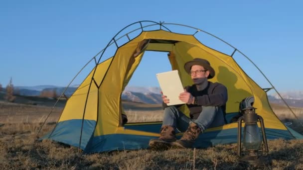 Genç adam turist turistik plaj 20'li yaşlarda 4 k çadırda oturan smartphone kullanarak gülümseyen — Stok video