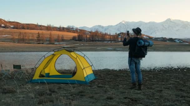 Young man taking a picture with smart phone in calm summer morning after night in red tent. Photo with space for your montage 20s 4k — Stock Video