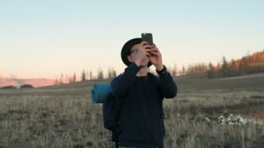 Genç adam akıllı telefon ile resim sakin yaz sabahı geceden sonra kırmızı çadırda alarak. Fotoğraf montaj 20'li yaşlarda 4 k için alan ile