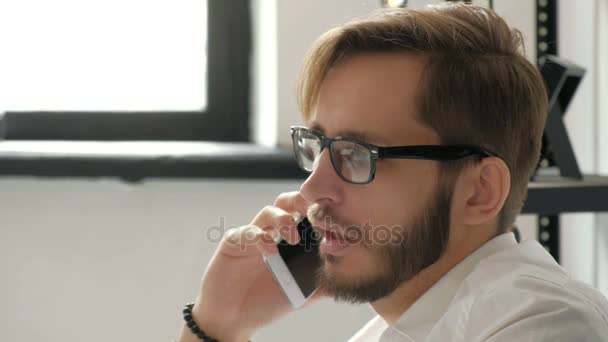 魅力的なヨーロッパの男職場 20 代 4 k でノート パソコンを使用しながら携帯電話で話しています。. — ストック動画