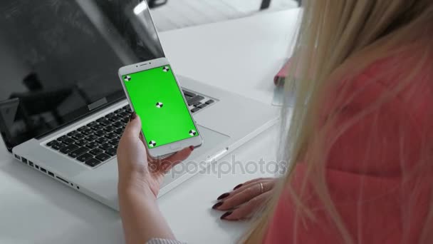Hände von oben betrachtet. Frau benutzt ihr Smartphone mit grünem Bildschirm in der Tabelle, scrollt Nachrichten, Fotos. Büro Schreibtisch Hintergrund. 20er Jahre 4k — Stockvideo