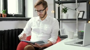 Resmi neşeli işadamı notları yazarken ofisinde oturuyor. Kameraya bakıyor. 20'li yaşlarda 4 k