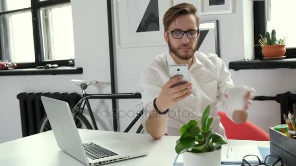 Hombre de negocios guapo está utilizando un teléfono inteligente y sonriendo mientras trabaja en la oficina 20s 4k — Vídeo de stock