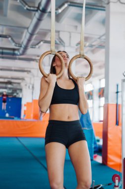 Genç, formda bir kadın jimnastik yüzüklerini çekiyor..