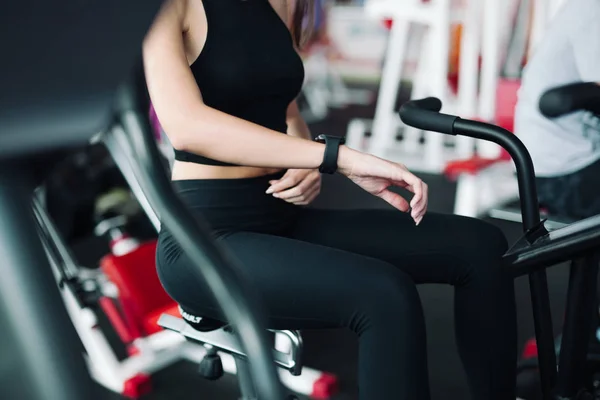 Mujer veinteañera usando reloj inteligente trabajando en bicicleta estática — Foto de Stock