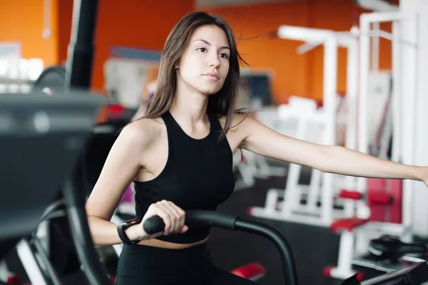 Jeune belle fille blanche en costume de sport est engagé sur un vélo stationnaire dans le club de fitness . — Photo