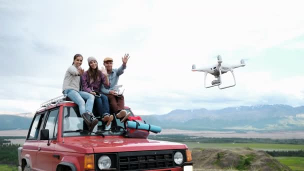 Gruppe von Freunden macht Selfie auf Drohne sitzt auf rotem Auto auf Bergkulisse Hintergrund 20s 4k. — Stockvideo