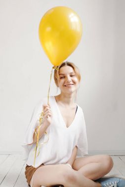 Sevimli kız gülümseyerek ve sarı balon ile arka plan boşaltmak ile oynarken bir stüdyoda portresi