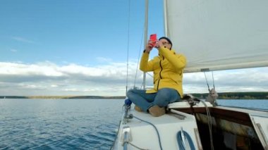 Yelkenli üzerinde oturan ve smartphone deniz arka plan üzerinde tarama genç adam.