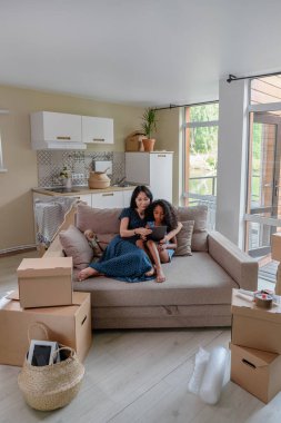 Gülümseyen anne ve onun sevimli küçük kızı oturma odası kanepede birlikte otururken dijital bir tablet üzerinde bir şey izlerken