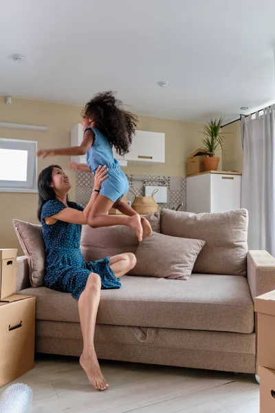 妈妈和女儿多种族搬到一个新公寓。 在沙发上跳来跳去玩吧. — 图库照片