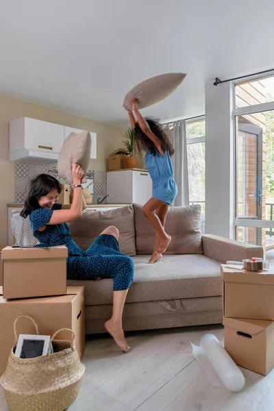 Anya és lánya multiracionálisok költöznek egy új lakásba. Jó ugrálást és játszadozást a kanapén.. — Stock Fotó